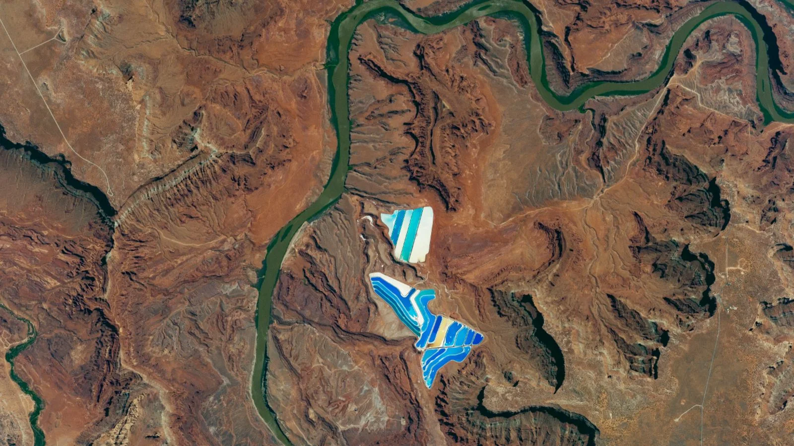 Blue solar ponds glow beside Utah’s river in space photo